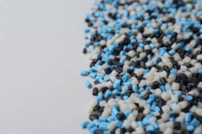 Elastómeros termoplásticos - Pila de gránulos de plástico de colores sobre fondo gris, primer plano.