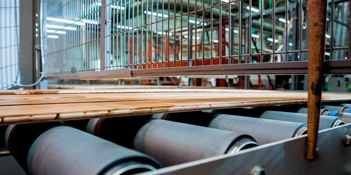 Recubrimiento de rodillos industriales en una línea de producción de una fábrica de pisos de madera.