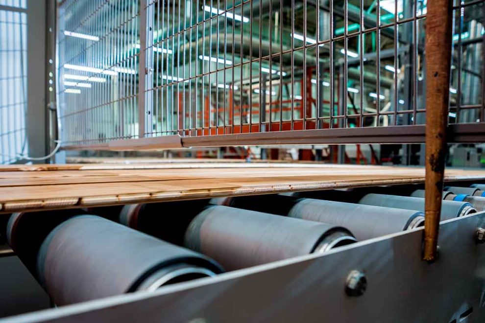Recubrimiento de rodillos industriales en una línea de producción de una fábrica de pisos de madera.